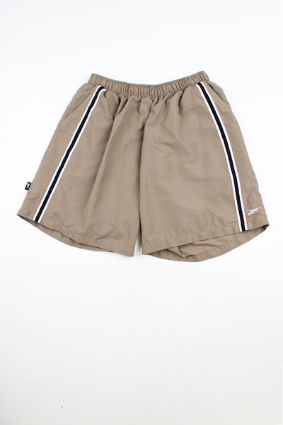 Tan Reebok shorts. Features embroidered patch logo on the back pocket.