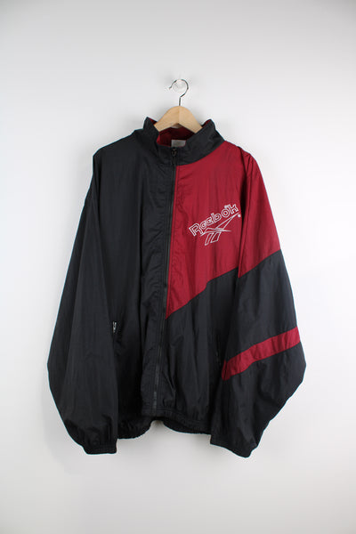 Vintage Reebok maroon red and black zip through nylon tracksuit jacket, features foldaway hood and embroidered spell-out logo on the chest