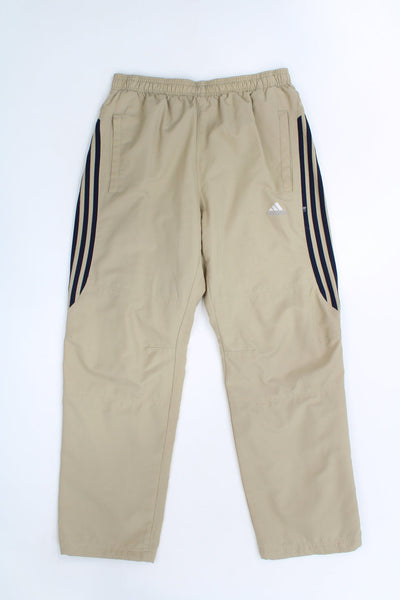 Tan Adidas tracksuit bottoms with embroidered logo on the hip and navy blue three stripes down legs 