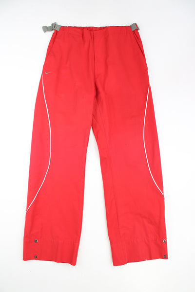 Y2K Nike red tech trouers with embroidered logo on the pocket and elasticated waistband at the back. The trousers also feature buckles at the side of the waistband to adjust the size slightly. They also have popper buttons at the cuffs to taper the leg. Size in Label: Womens L 