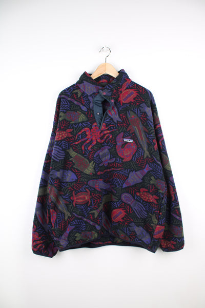 Vintage 1996 Patagonia Deep Under Synchilla Fleece in a purple, black and green colourway, quarter button up, animal patterned designs throughout, side pockets and has the logo embroidered on the front.