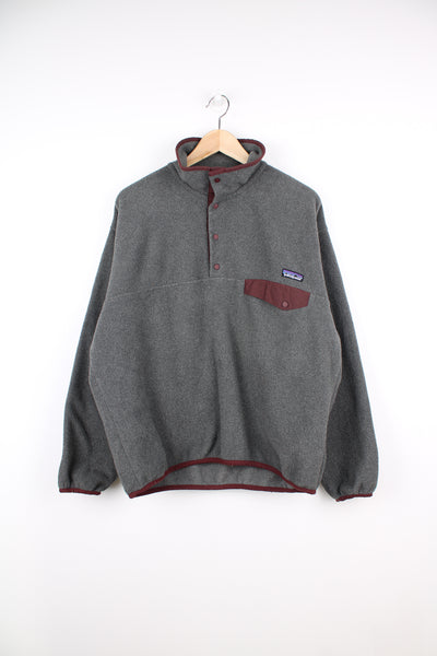 Patagonia Synchilla Fleece in a grey and burgundy colourway, quarter button up, chest pocket and has the logo embroidered on the front.