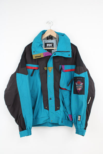 Vintage 90's teal blue and black Helly Hansen Ski Equipe jacket with embroidered badges on the sleeve and collar