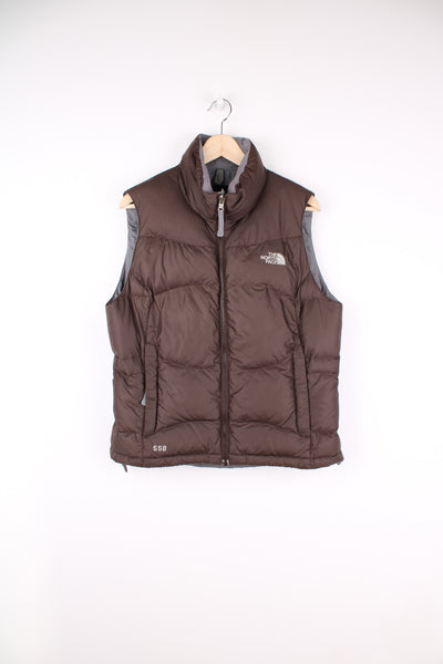 The North Face Face puffer gilet in brown, zip up with side pockets, insulated and has logo embroidered logo on the front and back.