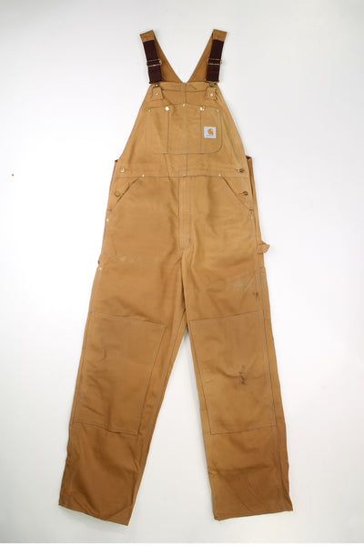 Vintage Carhartt tan denim dungarees with double knee reinforcement. Feature embroidered logo patch on the chest. good condition - marks throughout (see photos)Size in Label: 36 x 30 - Would estimate a Mens L