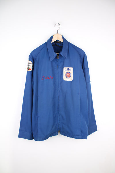 Vintage 1960's delivery drivers jacket from Miller High Life. Features embroidered patches for Miller High Life beer and has chain stitched "Ralph"  on the chest,. Lightweight jacket made from a blue Rayon material, has two front pockets and closes with a full zip. The jacket has a zip inside where it used to have a removable lining (this is missing). 
