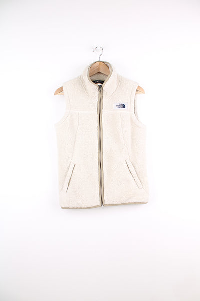 The North Face Fleece Vest in a white colourway, zip up, side pockets, and has the logo embroidered on the front.