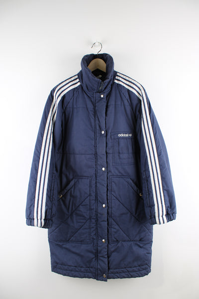 Vintage Adidas long puffer coat in blue with white stripes going down the sleeves, zip up with a hidden hood, multiple pockets, insulated and has logo embroidered on the front. 