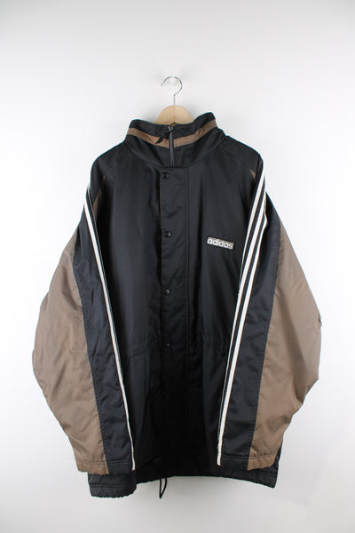 Vintage Adidas jacket in a black and brown colourway, has white stripes going down the sleeves, zip up, hidden hood and has logo embroidered on the front. 