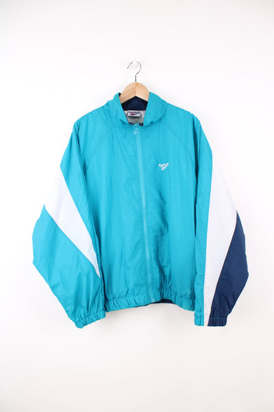 Reebok Shell Jacket in a blue and white colourway, zip up, side pockets, logo block pattern on the back as well as being embroidered on the front.