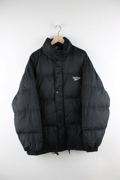 Vintage Reebok puffer jacket in black, zip up, insulated, side pockets and has the logo spell-out embroidered on the front and back.