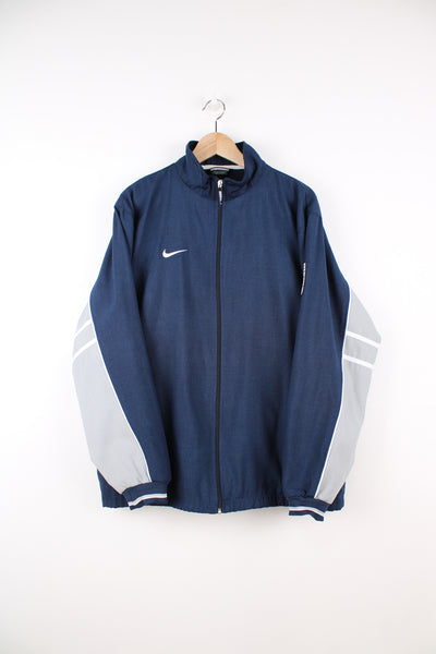 Nike Tracksuit Jacket in a navy blue and grey colourway, zip up, side pockets, and has the swoosh logo embroidered on the front.
