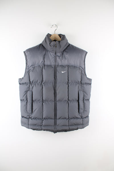 Vintage Nike padded gilet in grey, zip up, insulated, hidden hood, and has swoosh logo embroidered on the front. 