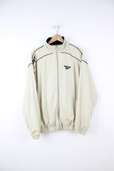 Reebok Tracksuit Jacket in a tan colourway, zip up, side pockets, and has the logo embroidered on the front.