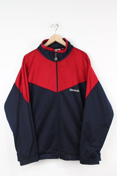 Navy blue and red Reebok zip through track jacket with embroidered logo on the chest and spell-out logo on the back