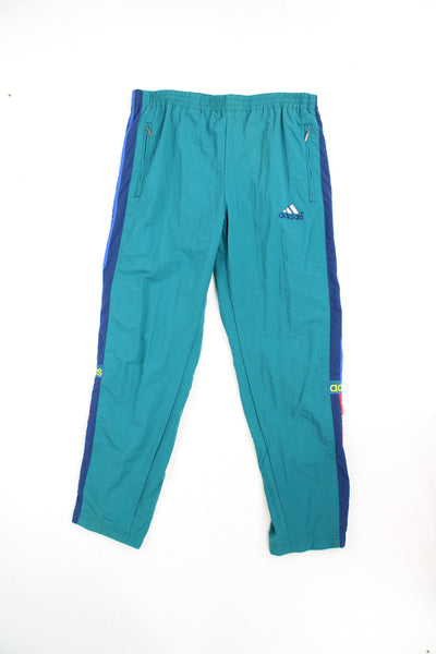 Vintage 90's Adidas tracksuit bottoms in turquoise blue with elasticated waistband and popper buttons down the legs. They also feature embroidered logos and three stripe detail. good condition Size in Label: 39 / 41 - Measure like a Mens XXL