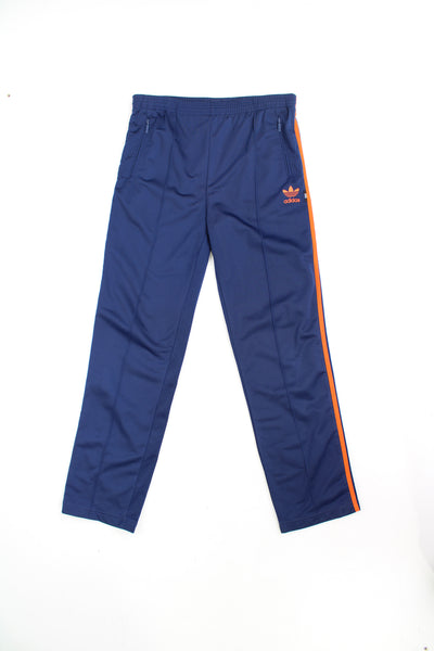 Vintage 90's Adidas tracksuit bottoms in blue with front seam detail and embroidered orange logo/ three stripe detail down the legs. good condition - elasticated waistband doesn't have much giveSize in Label: 30 - 32 - Measures like a Mens M