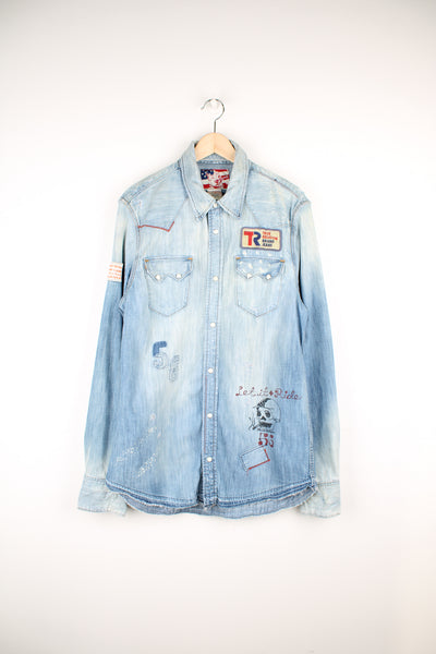 True Religion light wash heavily distressed denim shirt features embroidered badge and printed traditonal tattoo style graphics all over 