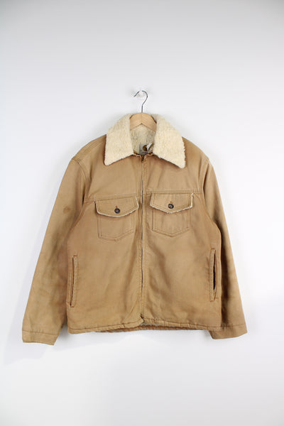 Vintage Carhartt Sherpa Workwear Jacket, in a tan colourway, sherpa lining and collar, multiple pockets, and has embroidered Carhartt logo on the front.