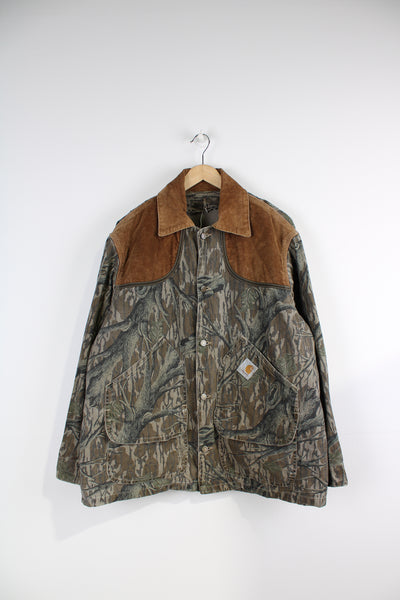 Vintage Carhartt Hunting / Shooting Workwear Jacket, in a Mossy Oak camo colourway, brown corduroy collar and shoulders, multiple pockets, and has embroidered Carhartt logo on the front.