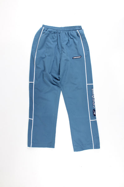 Reebok Tracksuit Bottoms in a blue colourway with white stipes and logo embroidered down the legs, and has a elasticated waist and pockets.