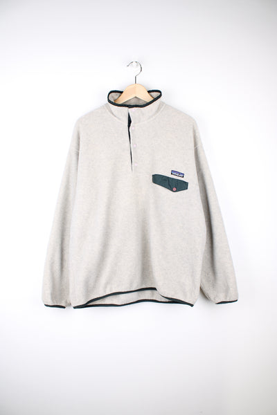 Patagonia Synchilla Fleece in a white and green colourway, quarter button up, chest pocket and has the logo embroidered on the front.