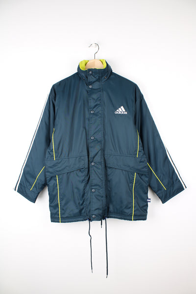 Vintage Adidas sports coat in dark teal blue, has white stripes going down the sleeves, hidden hood, adjustable waist and logo embroidered on the front.