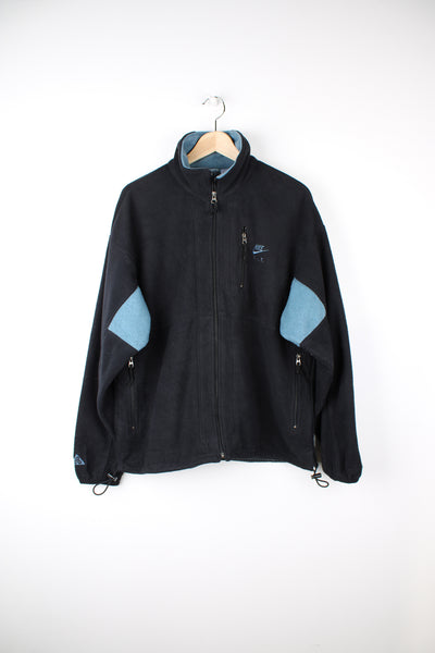 Nike ACG Fleece in a black and blue colourway, zip up, multiple pockets and has the logo embroidered on the front.
