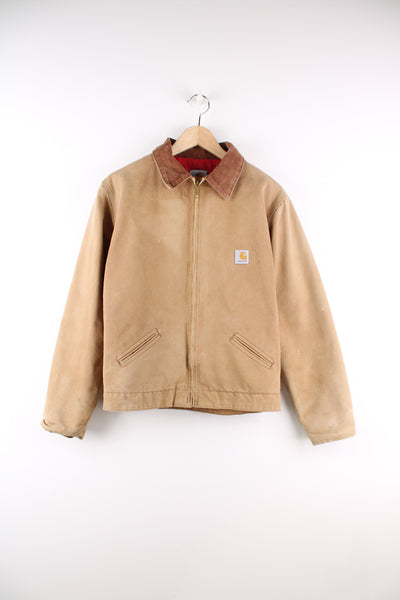 Carhartt Detroit Jacket in a tanned colourway with a brown corduroy collar, zip up, side pockets, red quilted lining, and has the logo embroidered on the front.