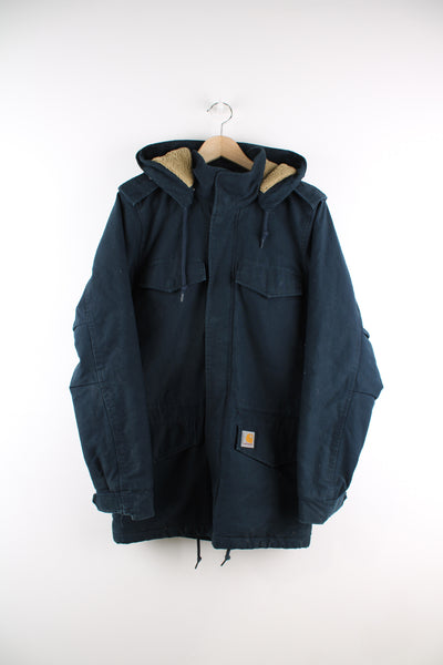 Carhartt Parka Jacket in a blue colourway, zip up, multiple pockets, detachable hood, sherpa lining, and has the logo embroidered on the front.