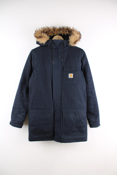 Carhartt Parka Jacket in a blue colourway, zip up, multiple pockets, hooded with a fox fur lining, quilted insulated lining, and has the logo embroidered on the front.