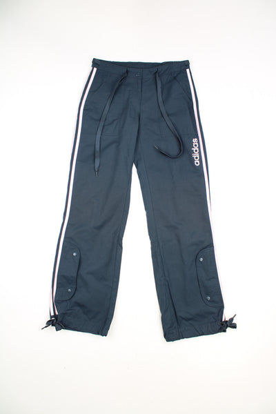 Adidas Tracksuit Bottoms in a navy blue colourway with pink three stripes going down the sides, adjustable waist, cargo style pockets, and has the logo spell out printed on the front.