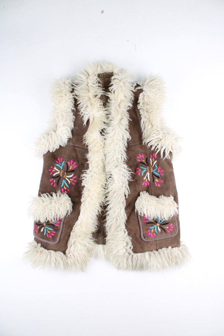Vintage Y2K Sheepskin Afghan Waistcoat in a brown colourway. This garment is worn loose and does not have a closure, has double pockets, fur lining and collar, and has floral patterns embroidered on the front and back.