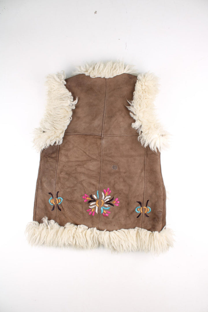 Vintage Y2K Sheepskin Afghan Waistcoat in a brown colourway. This garment is worn loose and does not have a closure, has double pockets, fur lining and collar, and has floral patterns embroidered on the front and back.