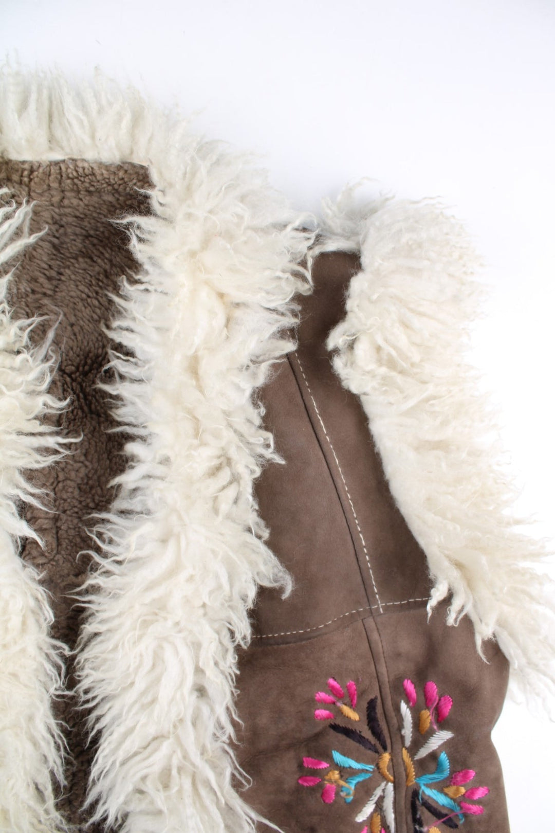 Vintage Y2K Sheepskin Afghan Waistcoat in a brown colourway. This garment is worn loose and does not have a closure, has double pockets, fur lining and collar, and has floral patterns embroidered on the front and back.