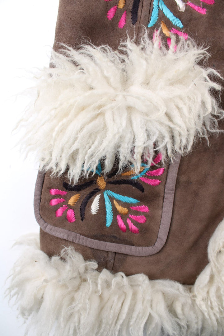 Vintage Y2K Sheepskin Afghan Waistcoat in a brown colourway. This garment is worn loose and does not have a closure, has double pockets, fur lining and collar, and has floral patterns embroidered on the front and back.
