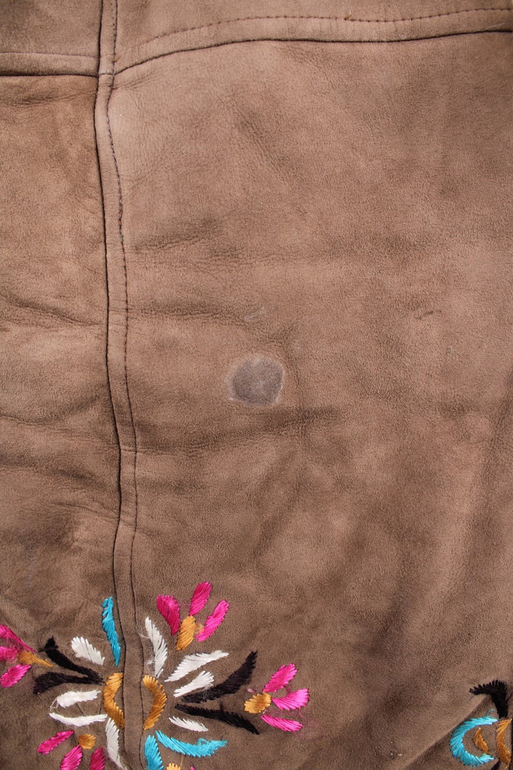 Vintage Y2K Sheepskin Afghan Waistcoat in a brown colourway. This garment is worn loose and does not have a closure, has double pockets, fur lining and collar, and has floral patterns embroidered on the front and back.