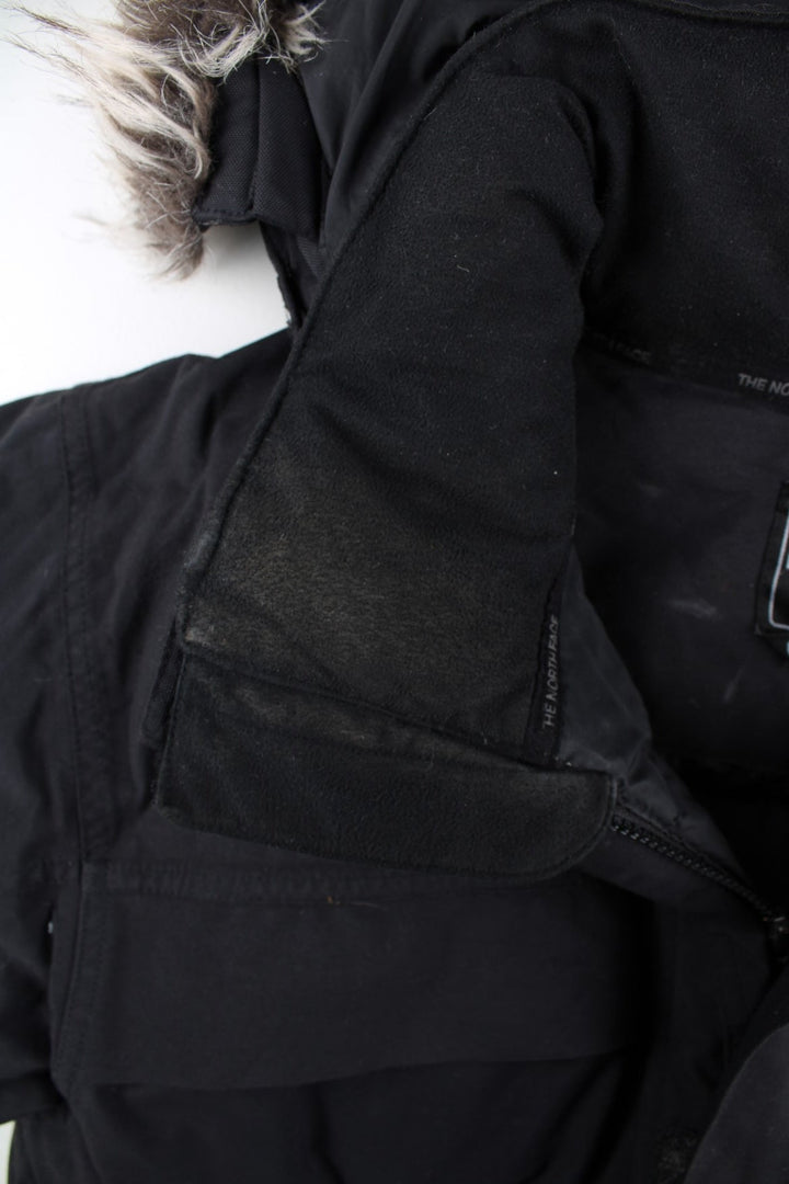 The North Face Parka Coat in a black colourway. Zips up and has multiple pockets, insulated lining, hooded with a detachable faux fur trim, and has the logo embroidered on the front and back.