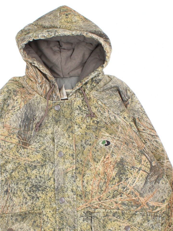 Vintage Russell Athletic Outdoors Mossy Oak Hooded Jacket in a green and green colourway. Zips up and has multiple pockets, insulated with a quilted lining, and has the logo embroidered on the front.