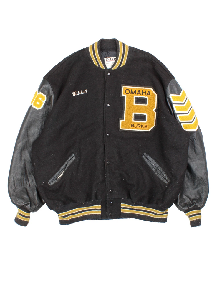 Vintage 'Omaha Burke' College Basketball Varsity Jacket in a black colourway with gold detailing. Classic varsity style with large lettering on the front and spell out on the back, buttons up with side pockets and leather sleeves.