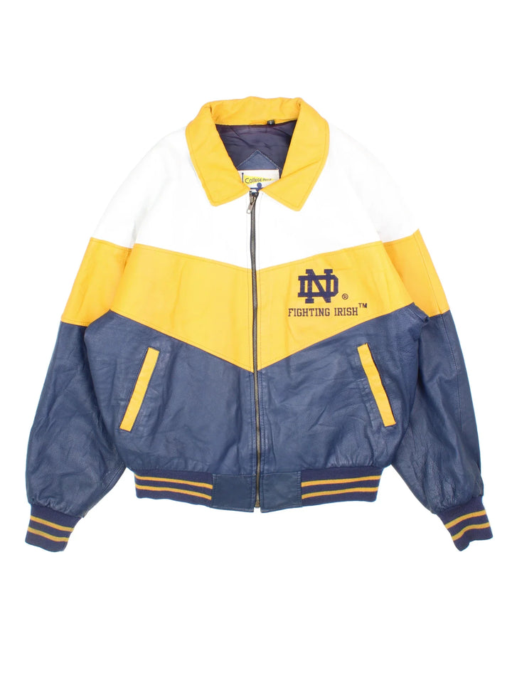 Vintage Notre Dame Fighting Irish Varsity Jacket in a blue colourway with white and yellow panelling. Full zip up and has side pockets, insulated lining, and has the logos embroidered on the front with large graphic on the back.