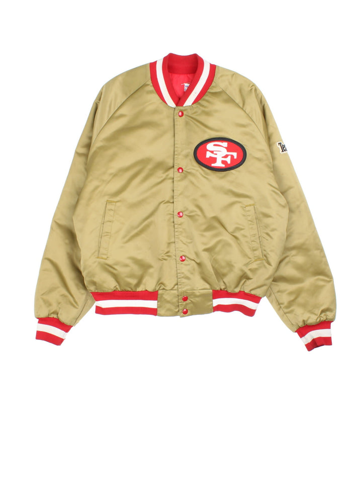 Vintage San Francisco 49ers NFL Chalk Line Varsity Jacket in a gold tan colourway. Buttons up and has side pockets, insulated with a quilted lining, and has the team logo and spell out embroidered on the front and back.