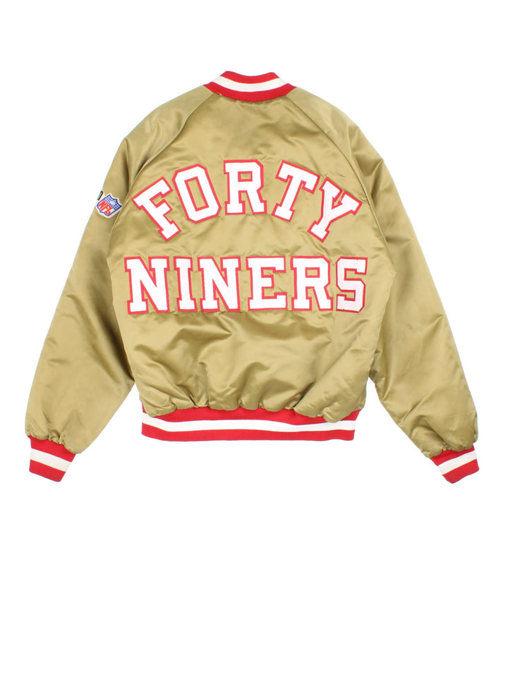 Vintage San Francisco 49ers NFL Chalk Line Varsity Jacket in a gold tan colourway. Buttons up and has side pockets, insulated with a quilted lining, and has the team logo and spell out embroidered on the front and back.