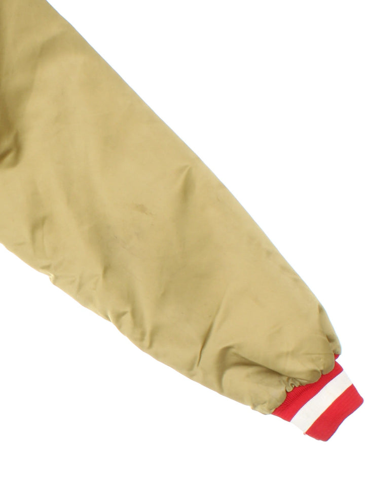 Vintage San Francisco 49ers NFL Chalk Line Varsity Jacket in a gold tan colourway. Buttons up and has side pockets, insulated with a quilted lining, and has the team logo and spell out embroidered on the front and back.