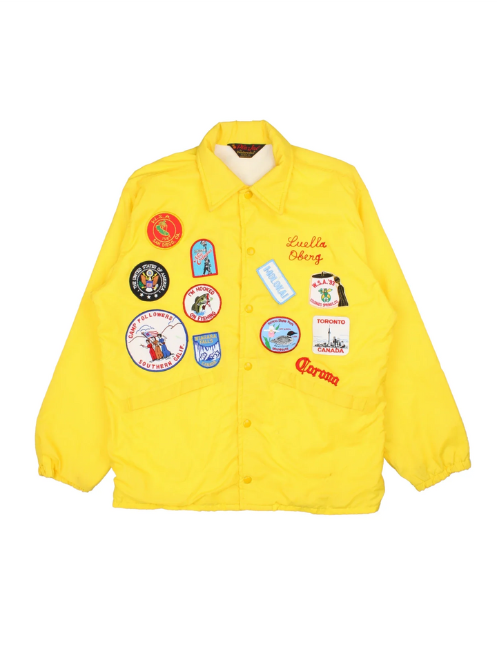 70's Vintage Coach Jacket in a yellow/multi colourway. Button popper fastening with front pockets, elasticated cuffs and hem with brushed lining. Embroidered patches and logos on front and back.