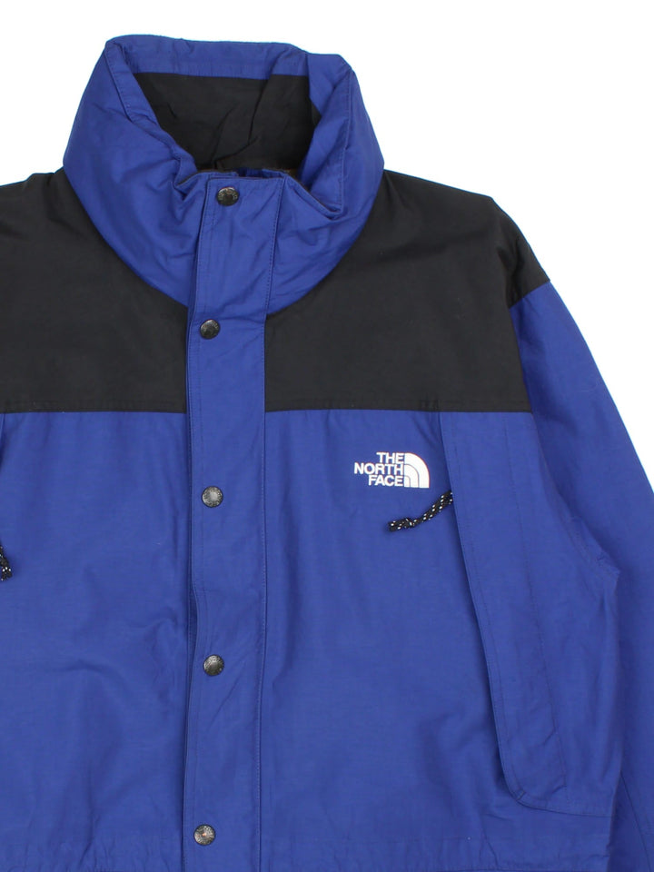 Vintage The North Face Mountain Jacket in a blue and black colourway. Zips an buttons up, has multiple pockets, hidden hood, and has the logo embroidered on the front and back.