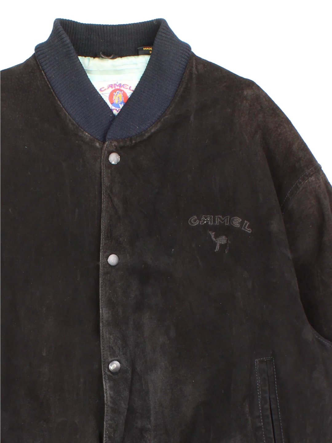 Vintage 90's Camel Suede Bomber Jacket in a black colourway. Buttons up and has side pockets, insulated with a satin lining, and has the logo embroidered on the front.