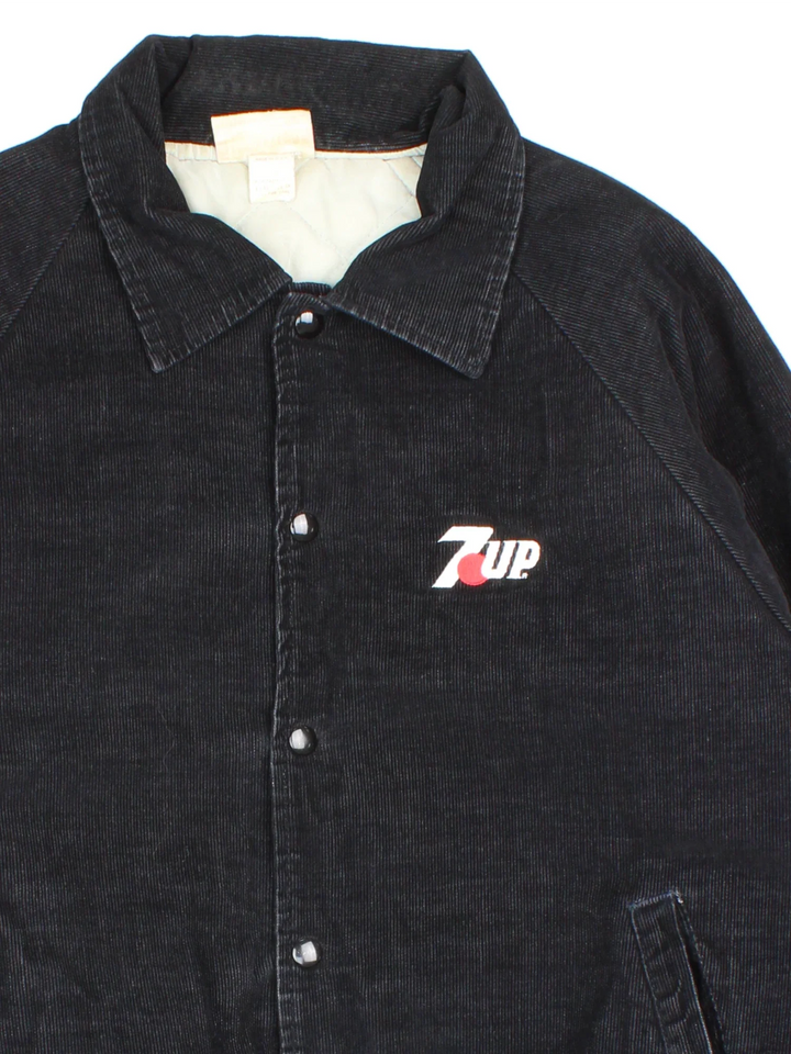 Vintage 1980's 7up Corduroy Jacket in a black colourway. Buttons up and has side pockets, insulated with a quilted lining, and has the logo embroidered on the front.
