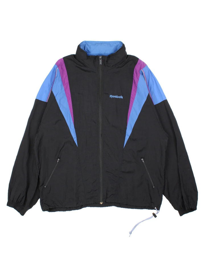 Vintage Reebok Tracksuit Jacket in a black colourway with blue and purple panelling, full zip up with multiple pockets and small logo on the chest.