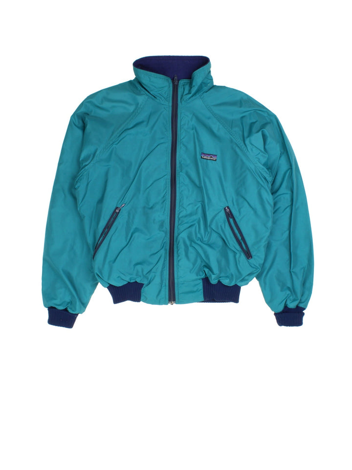 Patagonia Fleece Lined Bomber Jacket in a green colourway with navy cuffed sleeves and hem. Full zip with double front pockets and small classic logo.